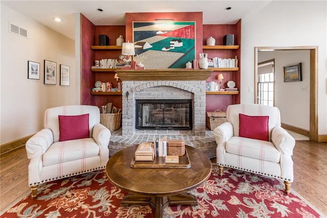 living room with visible vents, baseboards, built in features, a fireplace, and wood finished floors