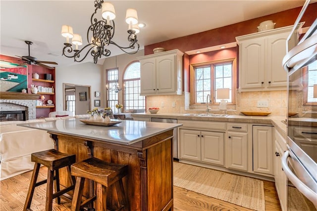 kitchen featuring a breakfast bar, a sink, a stone fireplace, ceiling fan with notable chandelier, and open floor plan