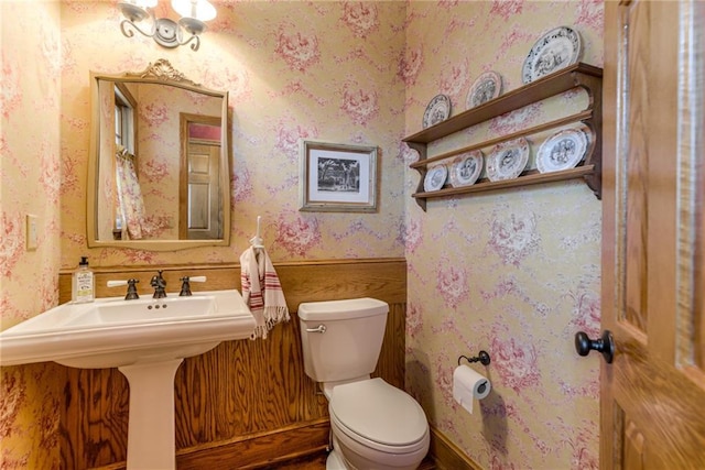 half bathroom featuring toilet, wallpapered walls, and a sink