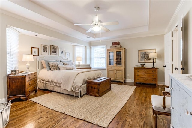 bedroom featuring baseboards, crown molding, a tray ceiling, and dark wood-style flooring