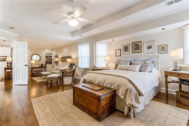 bedroom with wood finished floors, visible vents, baseboards, crown molding, and a raised ceiling