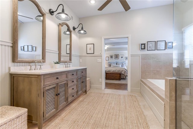 full bath with a wainscoted wall, double vanity, a sink, ceiling fan, and a bath