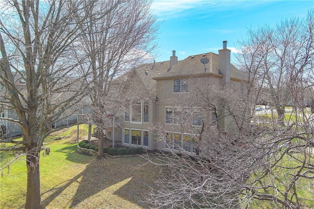 rear view of house featuring stucco siding, a lawn, a chimney, and stairway