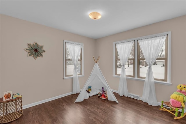 recreation room with dark wood-style floors, baseboards, visible vents, and a healthy amount of sunlight