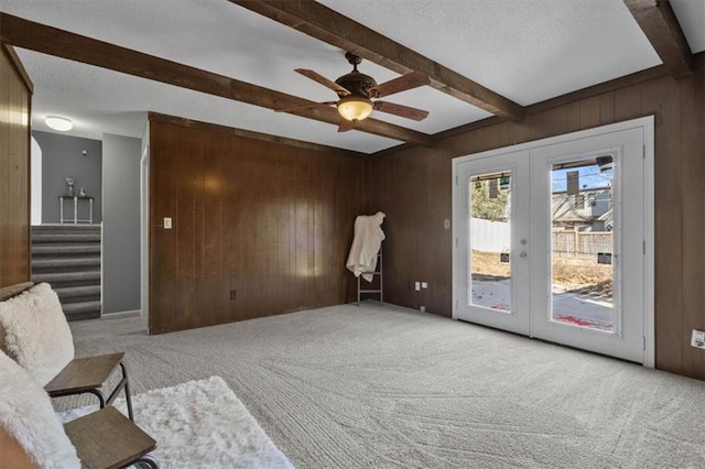 carpeted living area with french doors, wood walls, beam ceiling, and stairway