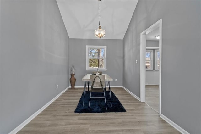 unfurnished dining area featuring vaulted ceiling, baseboards, and wood finished floors