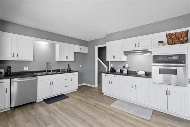 kitchen featuring dark countertops, stainless steel appliances, under cabinet range hood, white cabinetry, and a sink