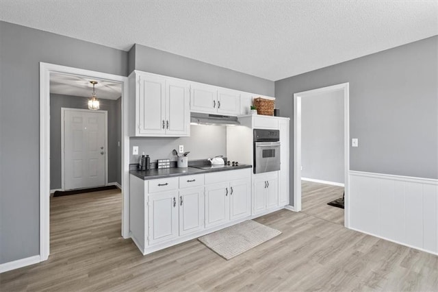 kitchen featuring white cabinets, dark countertops, oven, light wood-type flooring, and under cabinet range hood