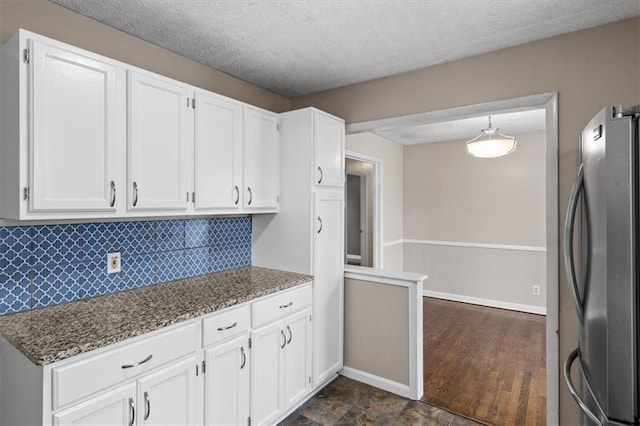 kitchen with hanging light fixtures, dark stone countertops, white cabinetry, and stainless steel fridge