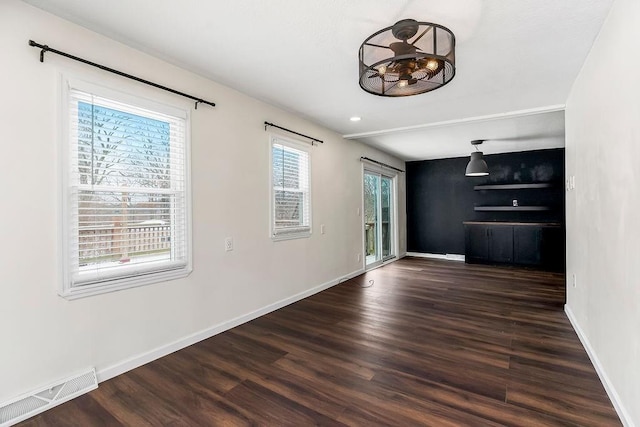 unfurnished living room with dark wood-type flooring, visible vents, and baseboards