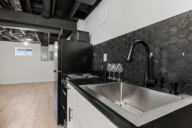 kitchen featuring electric panel, white cabinets, a sink, light wood-style floors, and backsplash