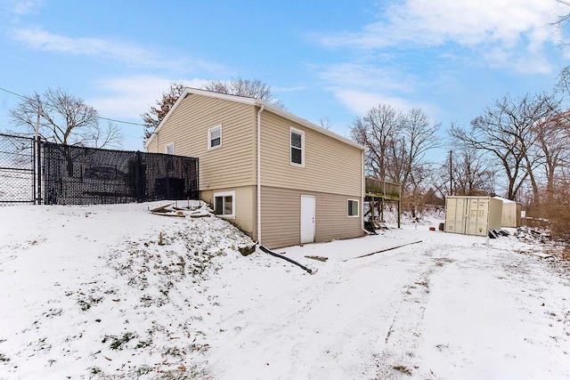 snow covered property featuring an outbuilding, a shed, and fence