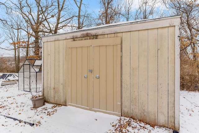 snow covered structure featuring an outbuilding and a storage unit