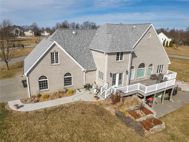 rear view of house featuring a wooden deck, a lawn, and a patio area