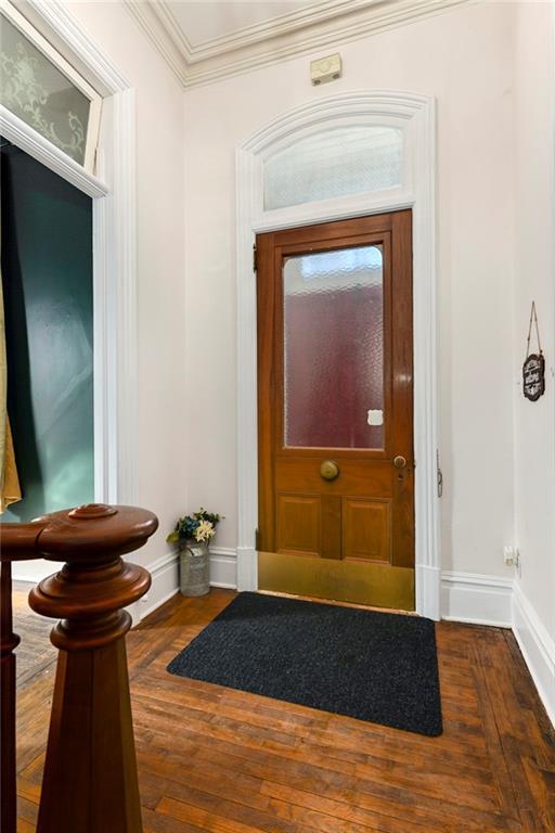 entryway with dark wood-style flooring, crown molding, and baseboards