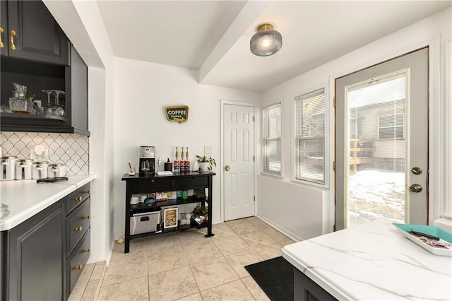 interior space featuring tasteful backsplash, baseboards, dark cabinets, and light tile patterned flooring