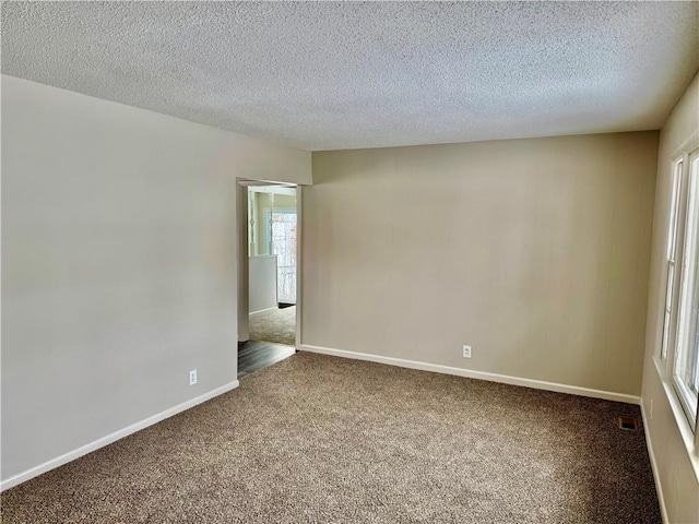 unfurnished room featuring dark colored carpet, visible vents, baseboards, and a textured ceiling