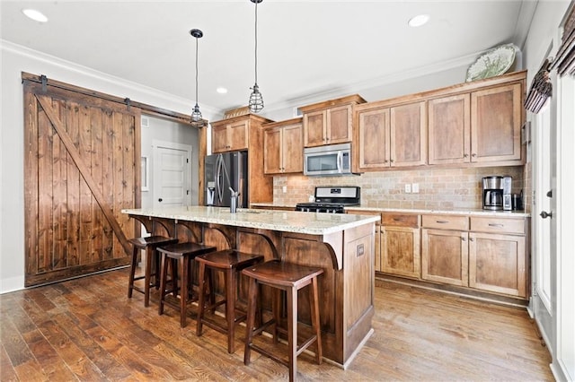 kitchen with a barn door, a kitchen island with sink, stainless steel appliances, hanging light fixtures, and ornamental molding