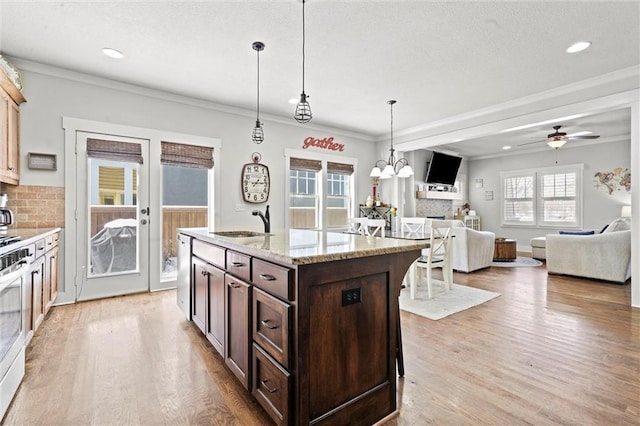 kitchen featuring dark brown cabinetry, open floor plan, hanging light fixtures, light stone countertops, and a sink