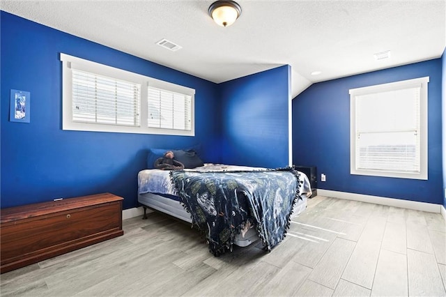 bedroom featuring a textured ceiling, visible vents, baseboards, vaulted ceiling, and light wood-style floors