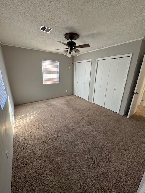 unfurnished bedroom featuring carpet floors, ornamental molding, ceiling fan, multiple closets, and a textured ceiling