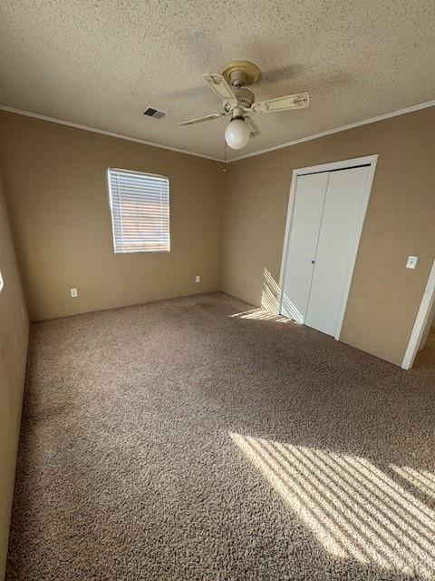 unfurnished bedroom featuring ceiling fan, ornamental molding, a textured ceiling, and carpet flooring