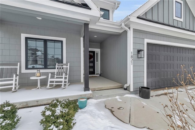 snow covered property entrance with a porch and a garage