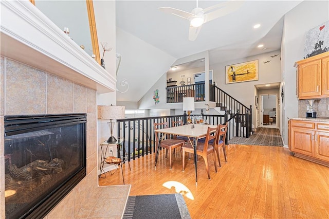 interior space with a fireplace, lofted ceiling, stairway, light wood-style flooring, and ceiling fan