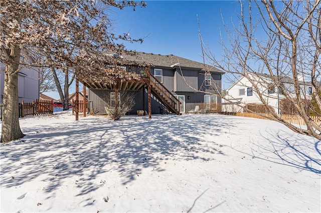 snow covered property featuring a deck, a residential view, fence, and stairway