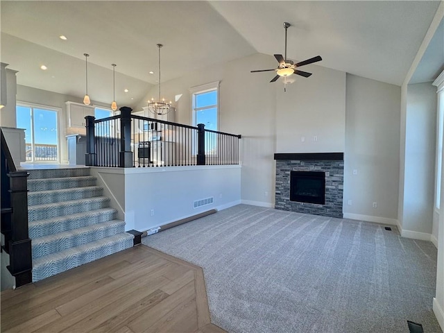 unfurnished living room featuring ceiling fan with notable chandelier, plenty of natural light, a stone fireplace, and high vaulted ceiling