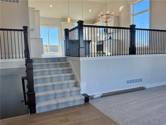 stairs featuring an inviting chandelier, hardwood / wood-style floors, and a towering ceiling