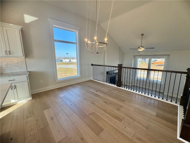 unfurnished dining area featuring ceiling fan with notable chandelier, vaulted ceiling, and light wood-type flooring