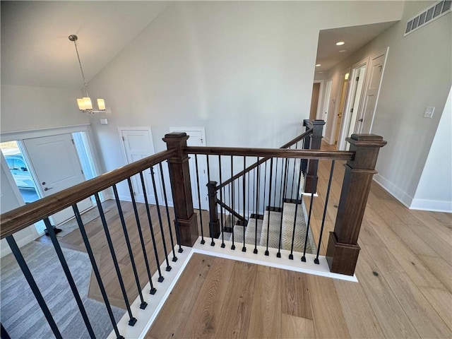 staircase with hardwood / wood-style floors, high vaulted ceiling, and a chandelier