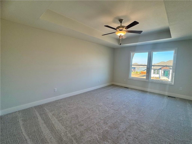 carpeted spare room with a tray ceiling and ceiling fan