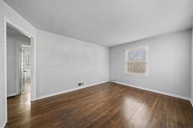 empty room featuring dark wood-style flooring, visible vents, and baseboards