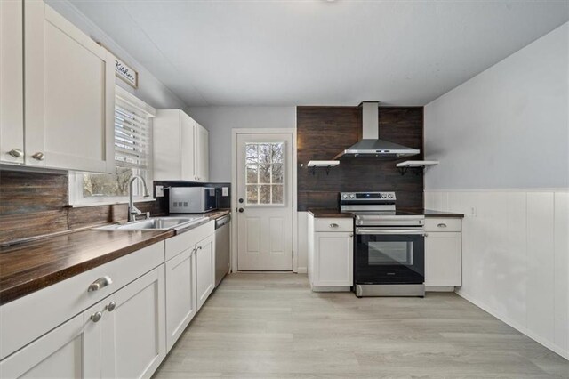 kitchen featuring appliances with stainless steel finishes, a healthy amount of sunlight, a sink, and wall chimney range hood