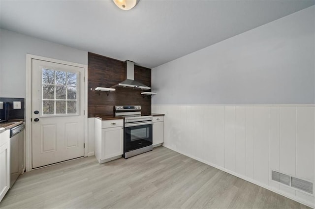 kitchen featuring stainless steel appliances, visible vents, wall chimney range hood, light wood-type flooring, and dark countertops