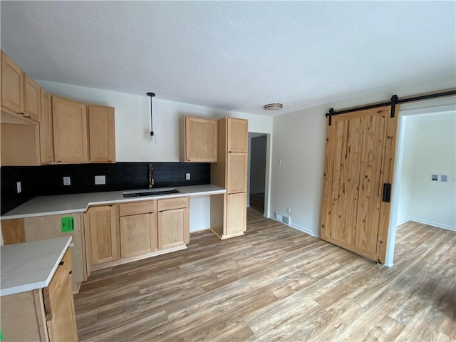 kitchen featuring sink, light hardwood / wood-style flooring, light brown cabinets, pendant lighting, and a barn door