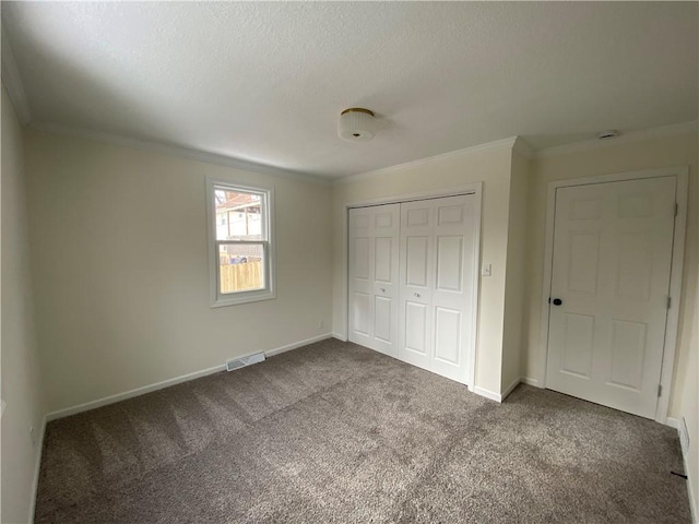 unfurnished bedroom featuring dark colored carpet, ornamental molding, a textured ceiling, and a closet