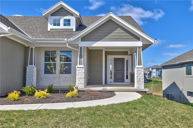 entrance to property featuring stone siding, a shingled roof, cooling unit, and a yard