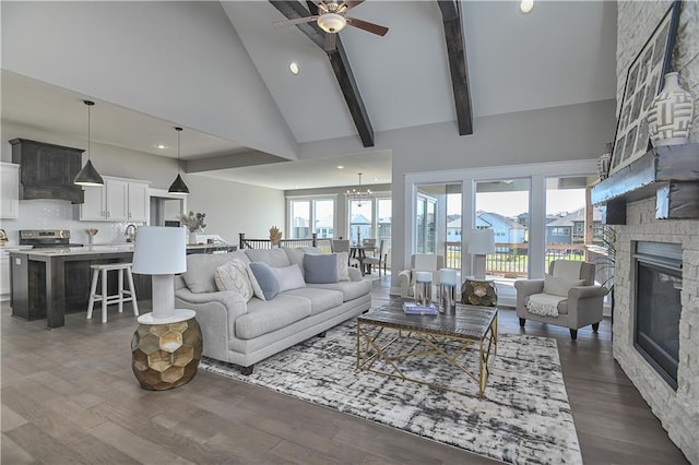 living area featuring high vaulted ceiling, dark wood-style flooring, a fireplace, a ceiling fan, and beamed ceiling