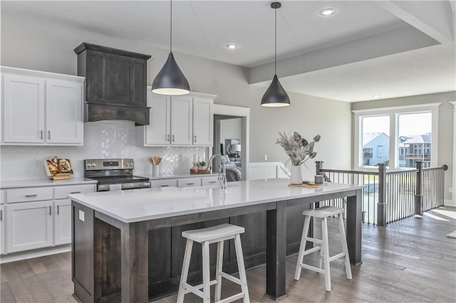 kitchen featuring wood finished floors, light countertops, decorative backsplash, and stainless steel range with electric cooktop