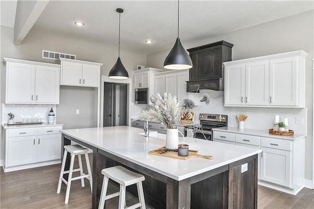 kitchen featuring stainless steel electric range oven, backsplash, white cabinets, an island with sink, and wood finished floors