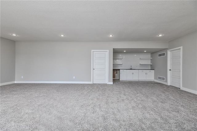 unfurnished living room with carpet floors, visible vents, a textured ceiling, and recessed lighting