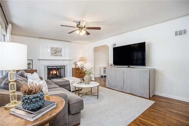 living area featuring a ceiling fan, wood finished floors, baseboards, a fireplace, and arched walkways