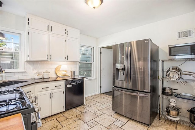 kitchen with appliances with stainless steel finishes, white cabinetry, backsplash, stone tile floors, and dark countertops