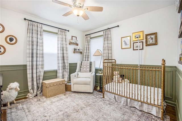 bedroom with a crib, a wainscoted wall, and ceiling fan