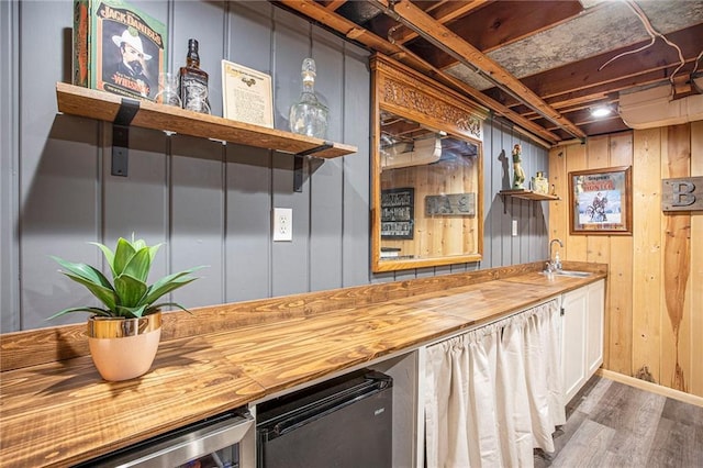 indoor bar featuring wood finished floors, beverage cooler, baseboards, and wood walls