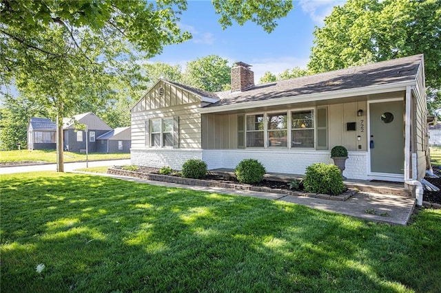 view of front of property with a chimney, a front yard, brick siding, board and batten siding, and a shingled roof