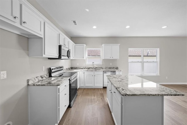 kitchen featuring a center island, light hardwood / wood-style flooring, stainless steel appliances, light stone countertops, and white cabinets